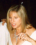 A blond-haired woman looks down to the ground. She wears a white dress and a silver necklace.
