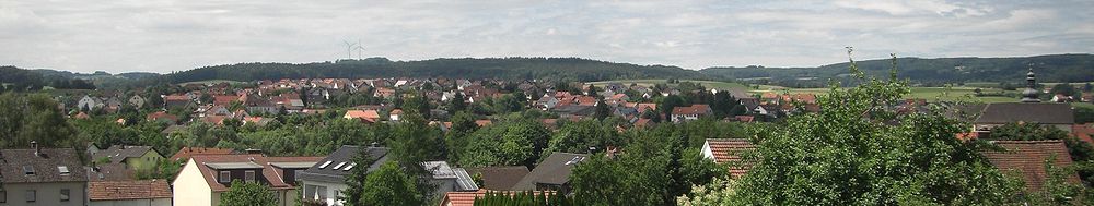 Das Panoramabild zeigt den Blick auf den südlichen Teil des Hauptortes aus Richtung Bahnhof/Eisenküppel. Im Hintergrund sind die beiden Windkrafträder zwischen Wallroth und Oberstork auf dem Gebiet der Stadt Schlüchtern zu erkennen, am rechten Bildrand die katholische Pfarrkirche St. Goar.