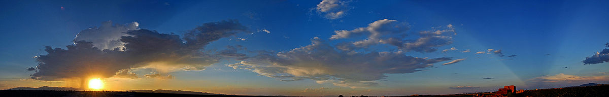~245°-Panoramabild eines Sonnenuntergangs bei Chandler (Arizona). Links neben der Sonne sind Fallstreifen zu sehen; die Regenwolke schattet die Sonne ab und erzeugt so Strahlenbüschel, die von Horizont zu Horizont bis in die Gegendämmerung im Osten reichen. Aufnahmedatum: 10. September 2005.