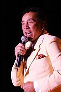 A man in a light-colored suit sings into a microphone