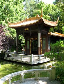 Chinesische Pagode mit geschwungenem Dach auf einer Steinplattform, die flach über ein Wasserbecken ragt