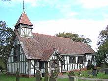 Eine kleine Fachwerkkirche mit einer Veranda und einem kleinen Kirchturm, einige Grabsteine im Kirchhof sind erkennbar.