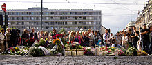 Foto einer Menschenmenge hinter niedergelegten Blumenkränzen und Kerzen