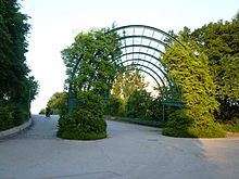 Ein teilweise mit Kletterpflanzen bewachsener, rund sechs Meter hoher Bogen aus einem Pseudo-3D-Stahlgerüst spannt sich über einen Fuß- und Radweg