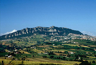 Blick von Osten. Das große Dorf am rechten Bildrand unterhalb der Steilwand ist Borgo Maggiore. Darüber ist auf dem Kamm die Festung La Guaita zu erkennen, die das Stadtzentrum von San Marino bildet.