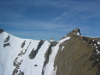 Sicht auf die Klimsen-Kapelle über dem Schneefeld des Nauen und das Klimsenhorn mit Gipfelkreuz.