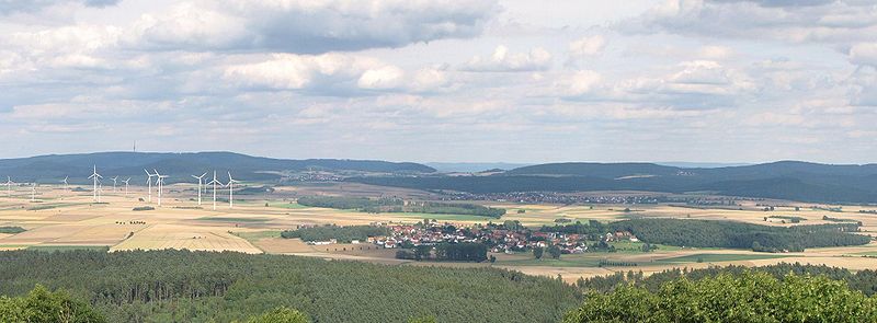 Blick von der Weidelsburg auf die Hoofer Pforte. Diese ist in der Bildmitte zu sehen. Links davon ist über den Windkraftanlagen der Hohe Habichtswald zu erkennen. Rechts des Passes liegen die Langenberge. Die Berge, die im Dunst durch den Pass zu sehen sind, liegen bereits östlich der Fulda und gehören zur Söhre.